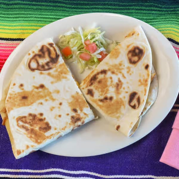 Two quesadilla halves with a side of shredded lettuce and diced tomatoes on a white plate.