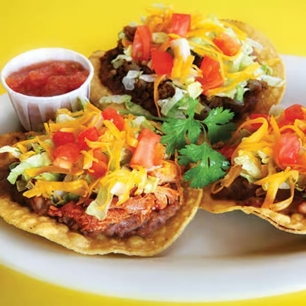 Three La Casita Mexican Grill tostadas with meat, cheese, lettuce, tomatoes, and a side of salsa.