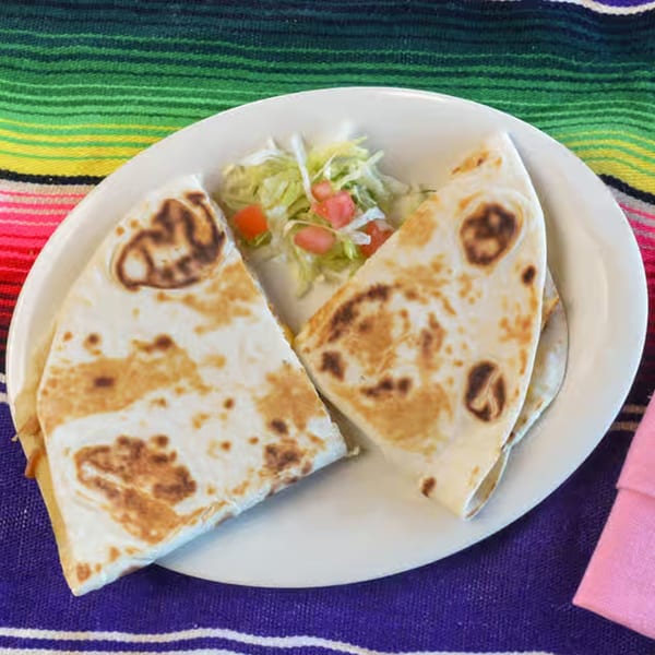 Two quesadilla halves and a side salad of shredded lettuce and diced tomatoes on a white plate.