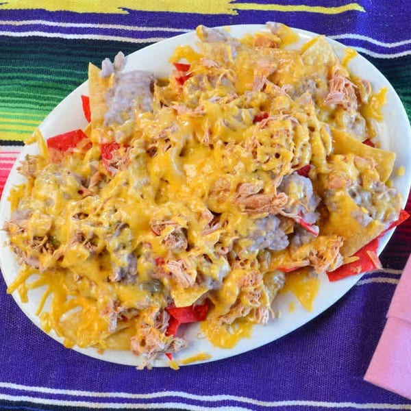La Casita Mexican Grill's nachos with melted cheese, shredded chicken, and red peppers on a colorful striped tablecloth.