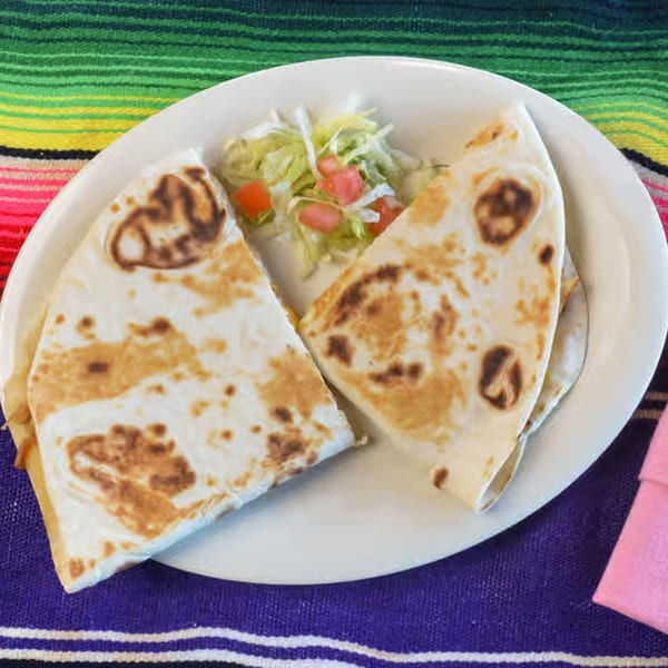 Two quesadilla halves with a side of shredded lettuce and diced tomatoes on a white plate.