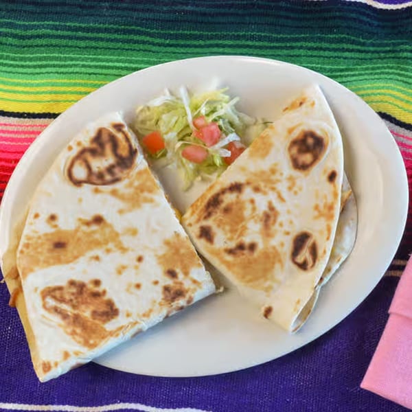 Two quesadilla halves with a side of shredded lettuce and diced tomatoes on a white plate.