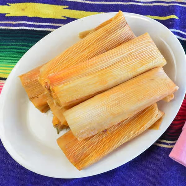 A white platter filled with several golden-brown tamales, resting on a vibrant, striped Mexican blanket.