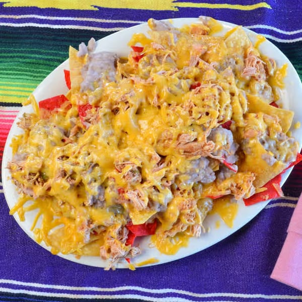 A plate of La Casita Mexican Grill's nachos with melted cheese, shredded chicken, and red peppers.