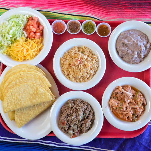 A Mexican feast with tacos, rice, beans, ground beef, shredded chicken, and various salsas.